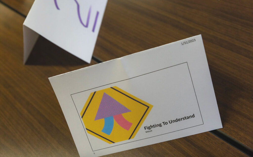 A white tent-fold card shows the Fighting to Understand logo and the words "Fighting to Understand (501(c)3."