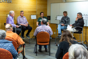 Five people sit in chairs in front of a small audence.